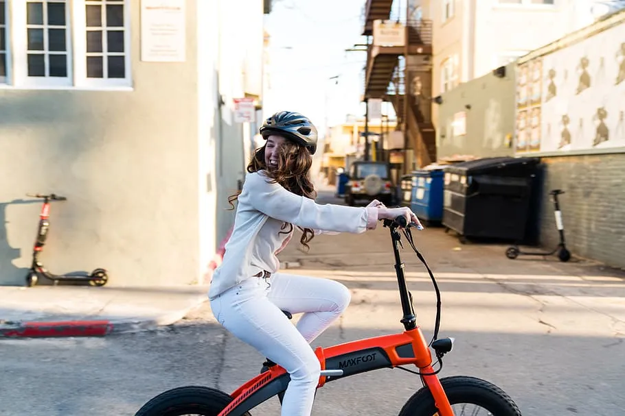 best electric cycle brands in india - a girl riding a orange foldable maxfcot e-bike.