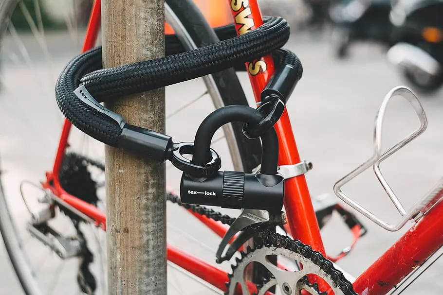 An Orange bicycle Locked with a bike lock.